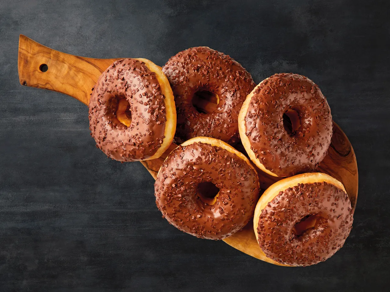 Schokoladen-Donuts mit bunten Streuseln auf einem Holzbrett.