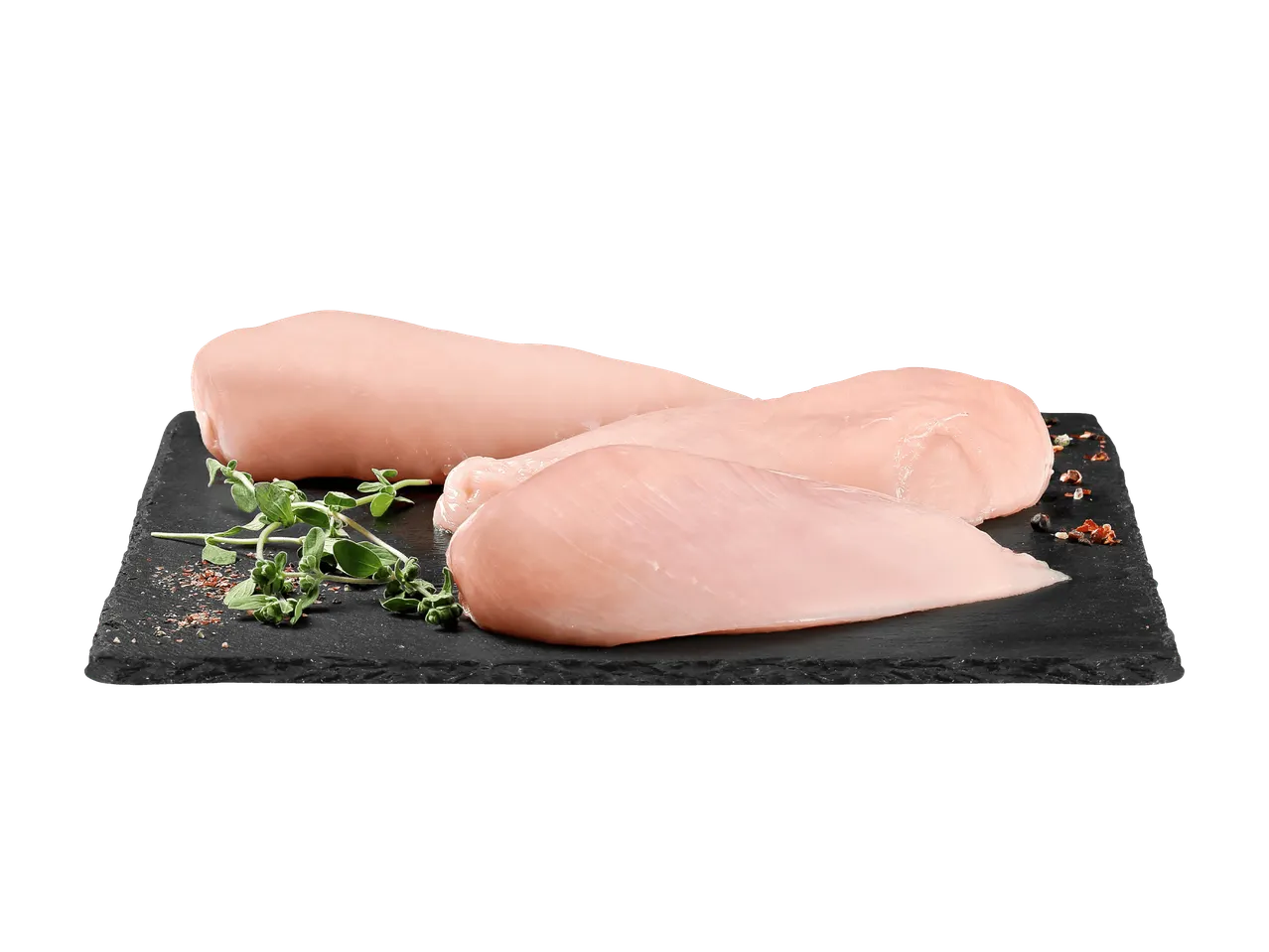 Filets de poulet crus sur une planche en ardoise noire avec des herbes et des épices.