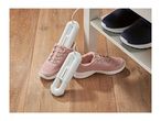 An electric shoe dryer inserted into pink sneakers on a wooden floor next to a shoe rack.