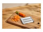 Carrot grater with a whole carrot and shredded carrots on a wooden cutting board.