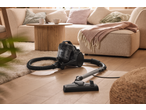 Vacuum cleaner on a wooden floor with a fluffy rug, next to a sofa and coffee table.