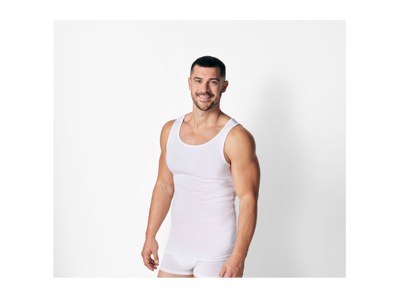 Smiling man in a white tank top and white boxer briefs.