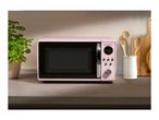 A pink SilverCrest microwave on a kitchen counter with a plant and wooden utensils.