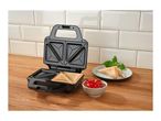Sandwich maker with toasted sandwiches, cherry tomatoes, and basil on a wooden counter.