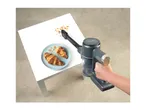 Handheld vacuum cleaning croissant crumbs off a white table next to a plate of croissants.