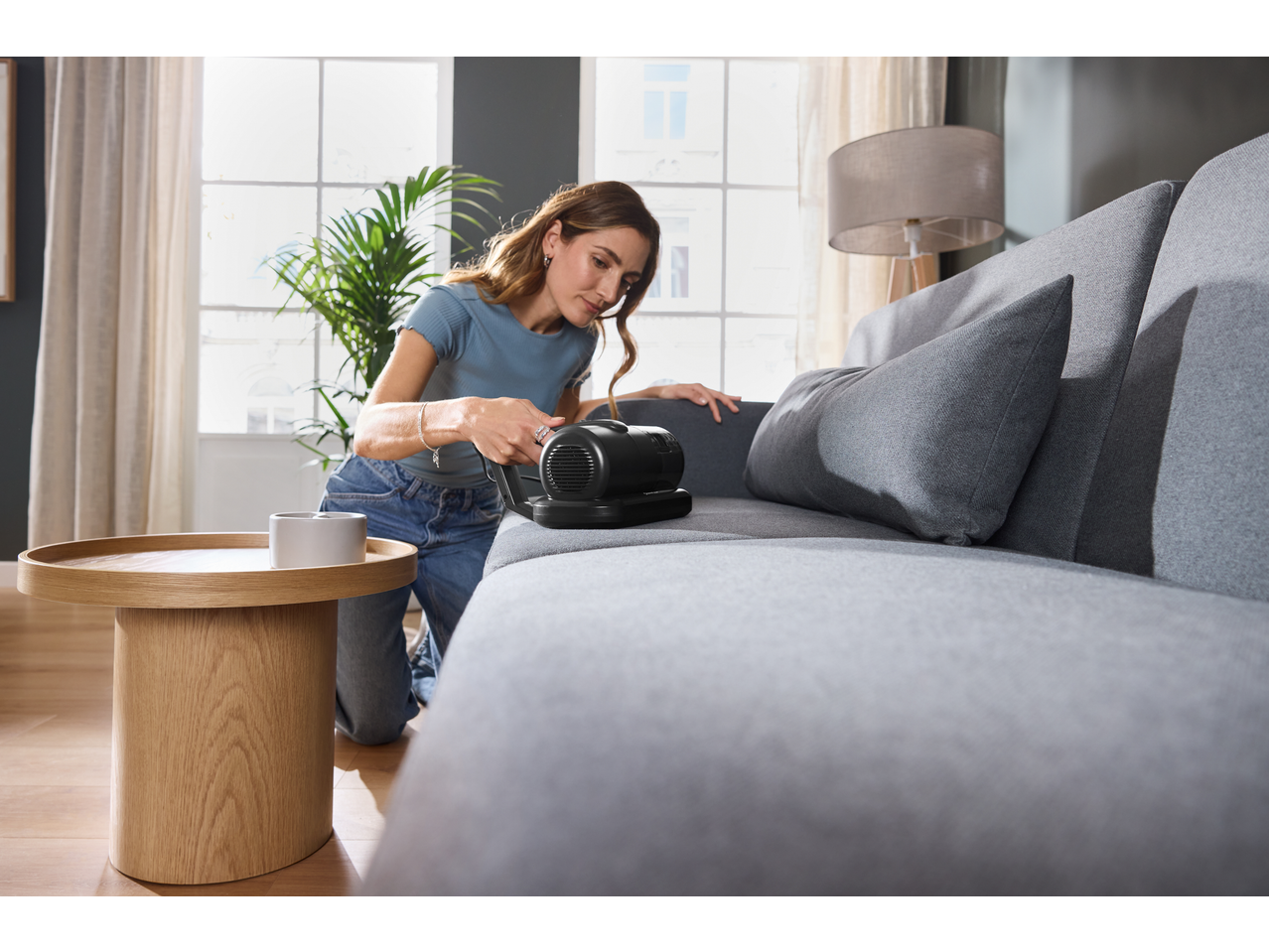 Femeie curățând o canapea gri cu un aspirator anti-acarieni SILVERCREST.
