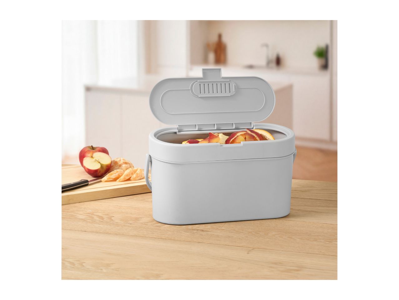 Grey kitchen waste bin filled with fruit peels on a wooden table.