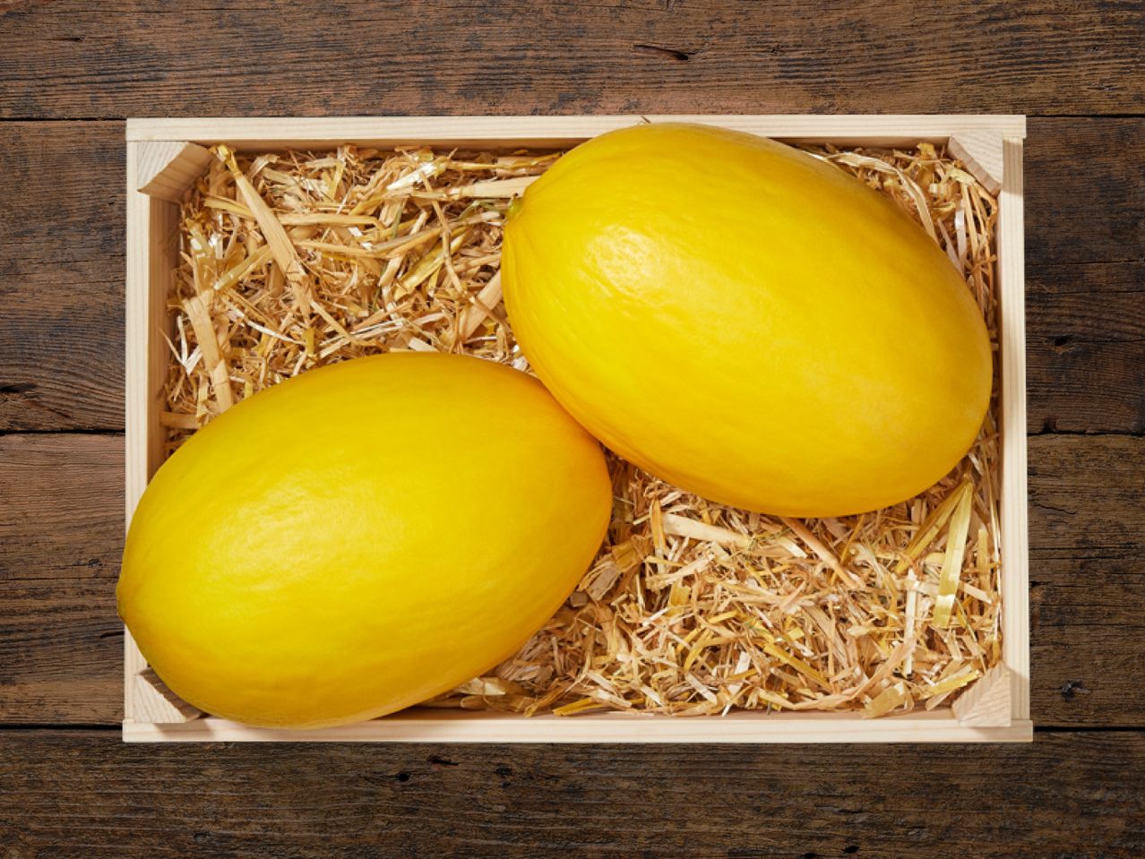Zwei gelbe Melonen in einer Holzkiste mit Stroh.