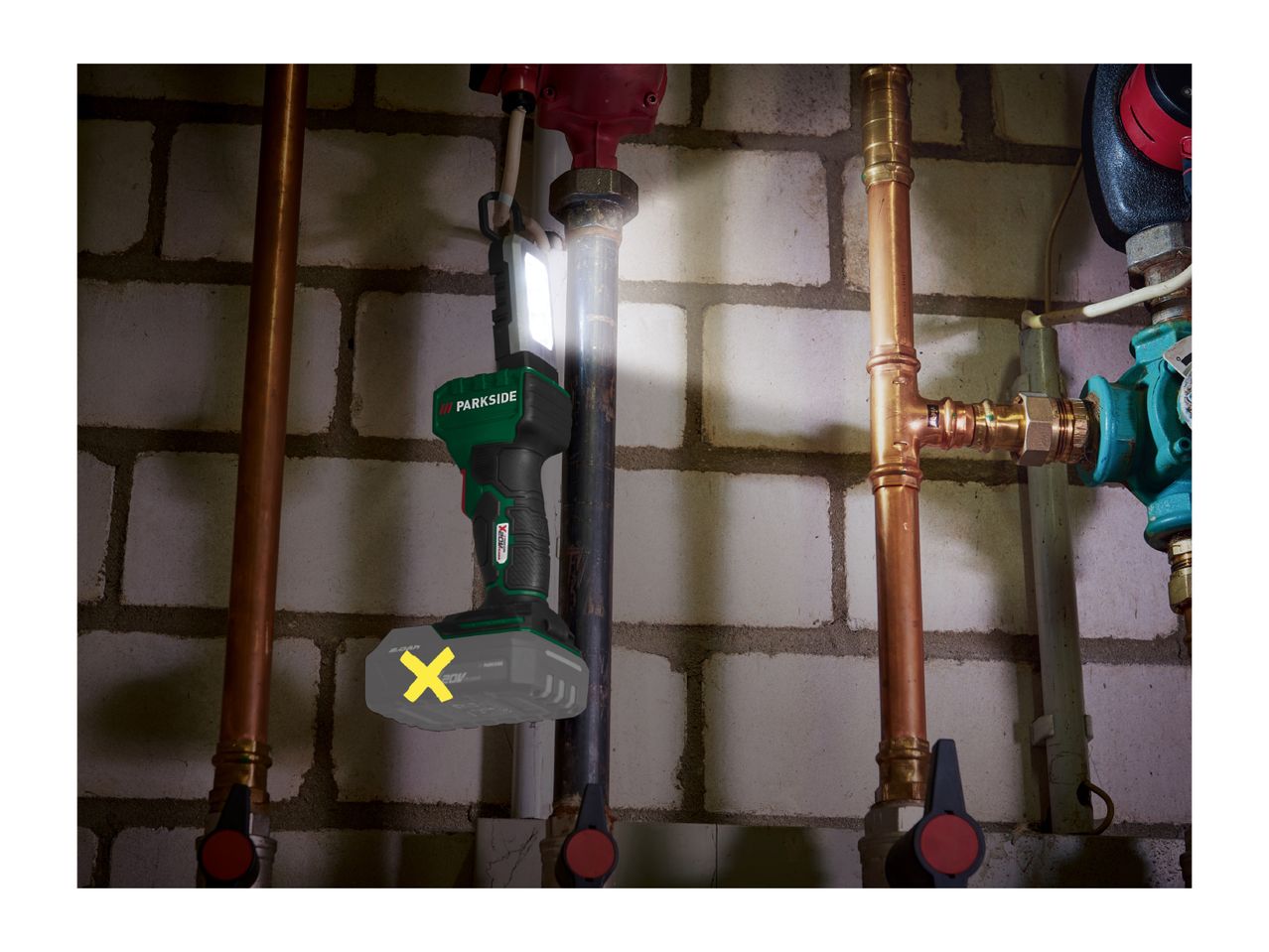 Cordless work light illuminating pipes and a brick wall in a basement setting.