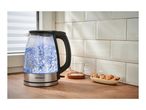 Glass kettle with boiling water, a glass mug, and chocolate chip cookies on a wooden counter.