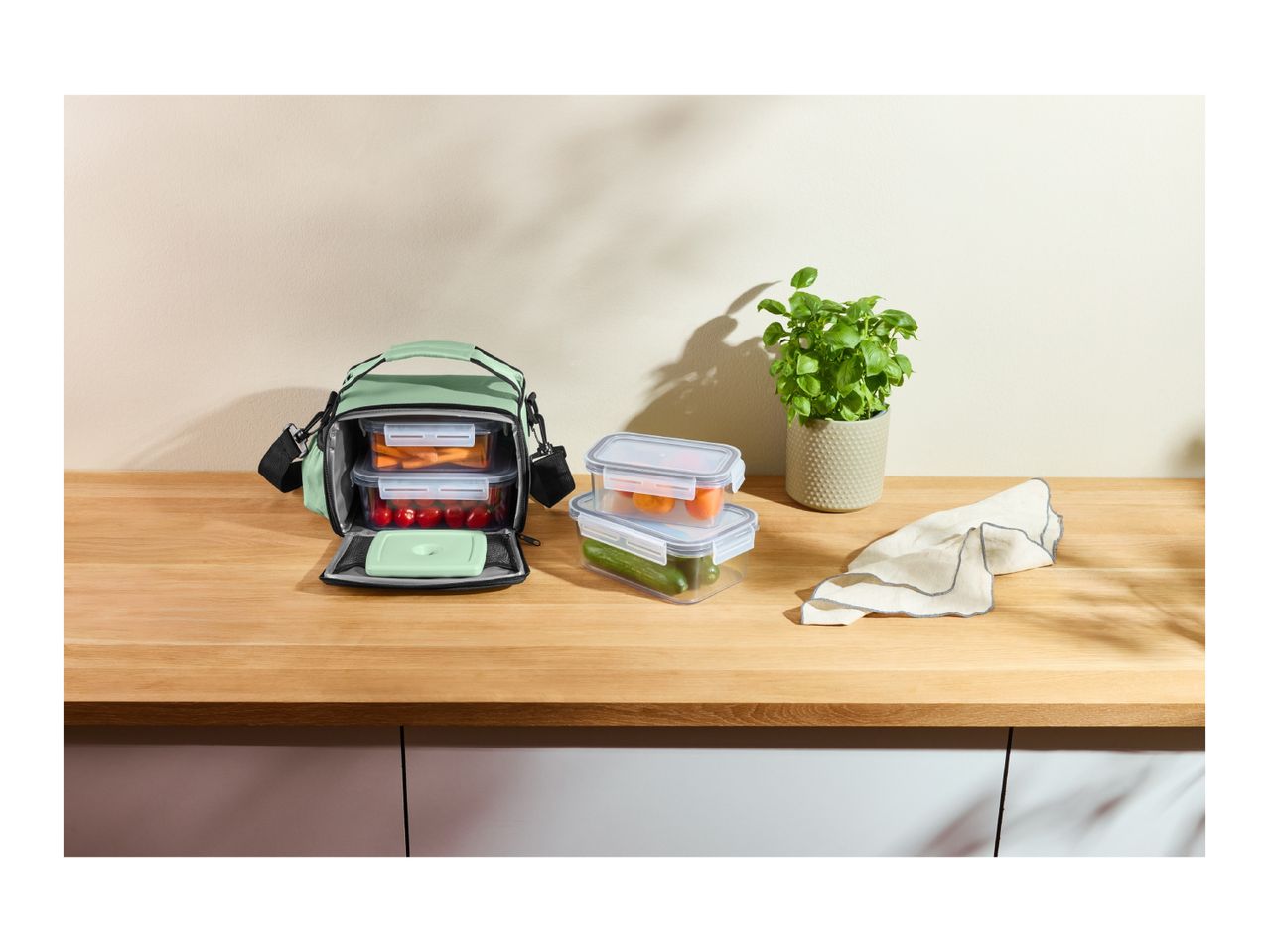 Green lunch bag with food containers filled with vegetables on a wooden counter.