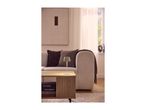 A modern, minimalist table lamp glowing on a wooden coffee table in a cozy living room.