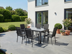 Conjunto de jantar exterior com mesa cinzenta e seis cadeiras num pátio junto a uma casa branca.