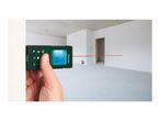 Hand holding a laser distance measurer, showing a measurement of 16.75m in an empty room.