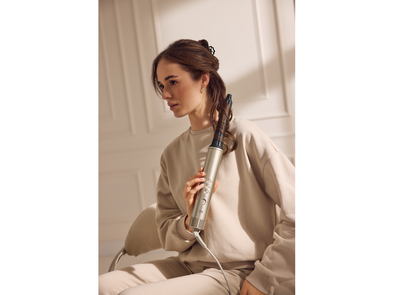 Woman styling her hair with a hair styler, creating a curl.