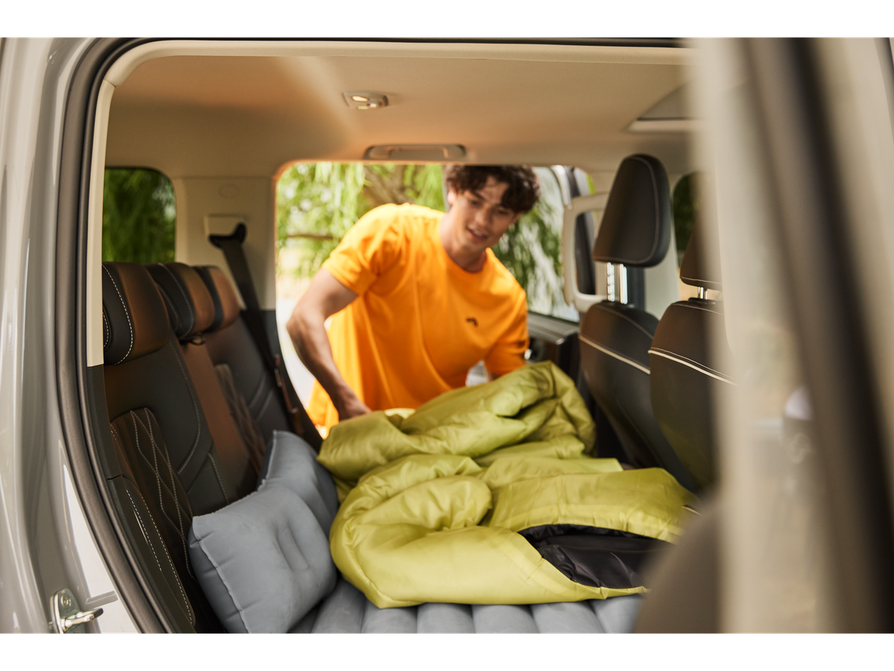 A man puts a sleeping bag and inflatable mattress in the back of an SUV.