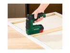 Hand using a green and black staple gun to stretch a canvas over a wooden frame.