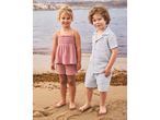 Two children in summer outfits on a beach, a girl in a pink top and shorts, a boy in a light blue shirt and shorts.