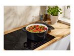 A black cast iron pot filled with vegetables on an induction cooktop.