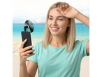 Mulher com telefone e ventoinha USB na praia.