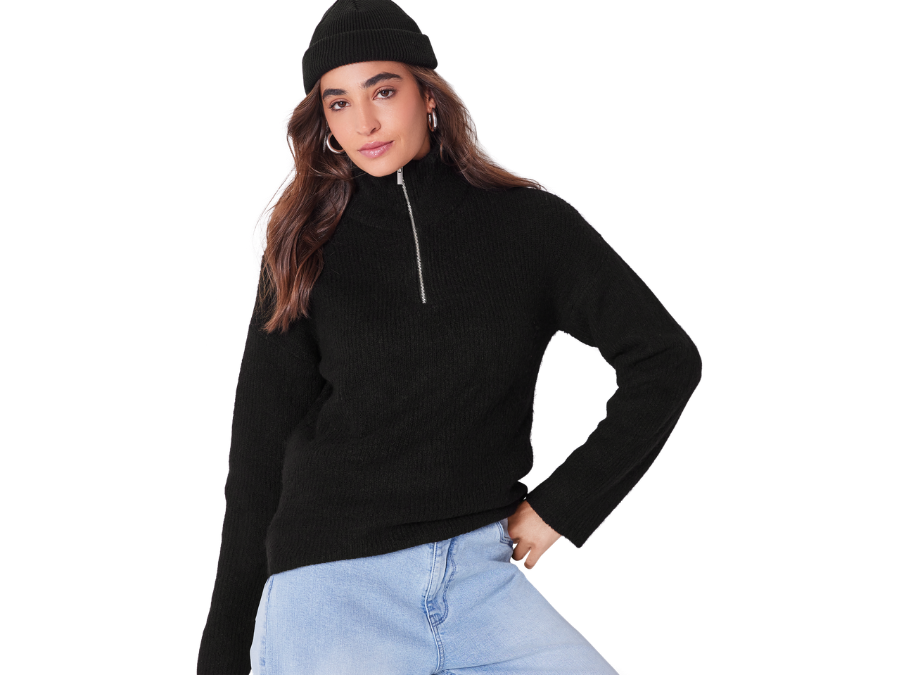 Moteris su juodu megztu džemperiu su užtrauktuku, kepure ir šviesiais džinsais.