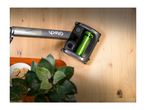 A cordless upright vacuum cleaner on a wooden floor next to a plant and cookies.