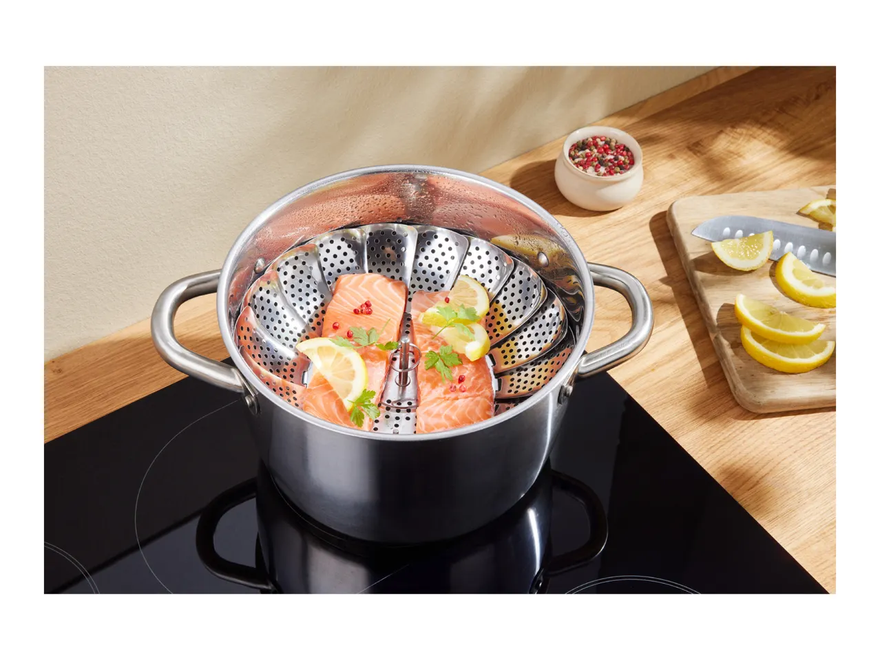 Salmon fillets with lemon and herbs in a steamer basket inside a pot on an induction hob.