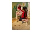 A young girl playing with a pink wooden toy dressing table and stool, decorated for Christmas.