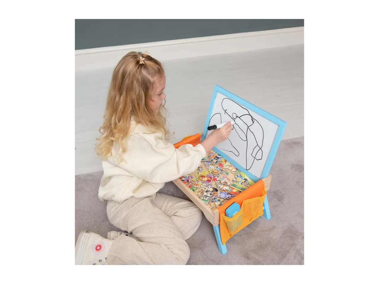 A child drawing on a tabletop easel with a whiteboard and magnetic letters.