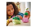 A smiling child plays with two colorful toy plant pots with faces, one green and one pink.
