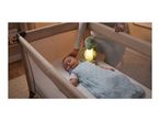 Baby sleeping in a cot with a glowing dinosaur night light and an adult's hand.