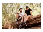 Two people in activewear sitting on a fallen log in a forest, smiling.