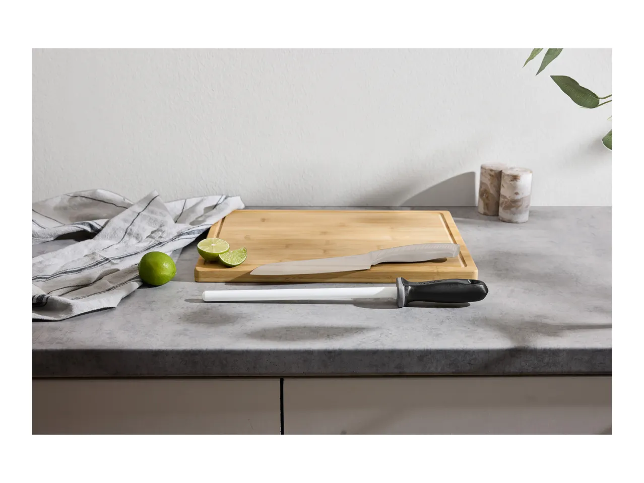 A ceramic knife sharpener and a chef's knife on a wooden cutting board with limes.