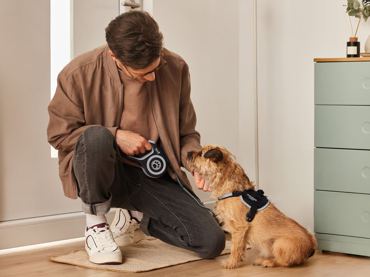 Man crouching, attaching a retractable dog leash to a dog wearing a harness.