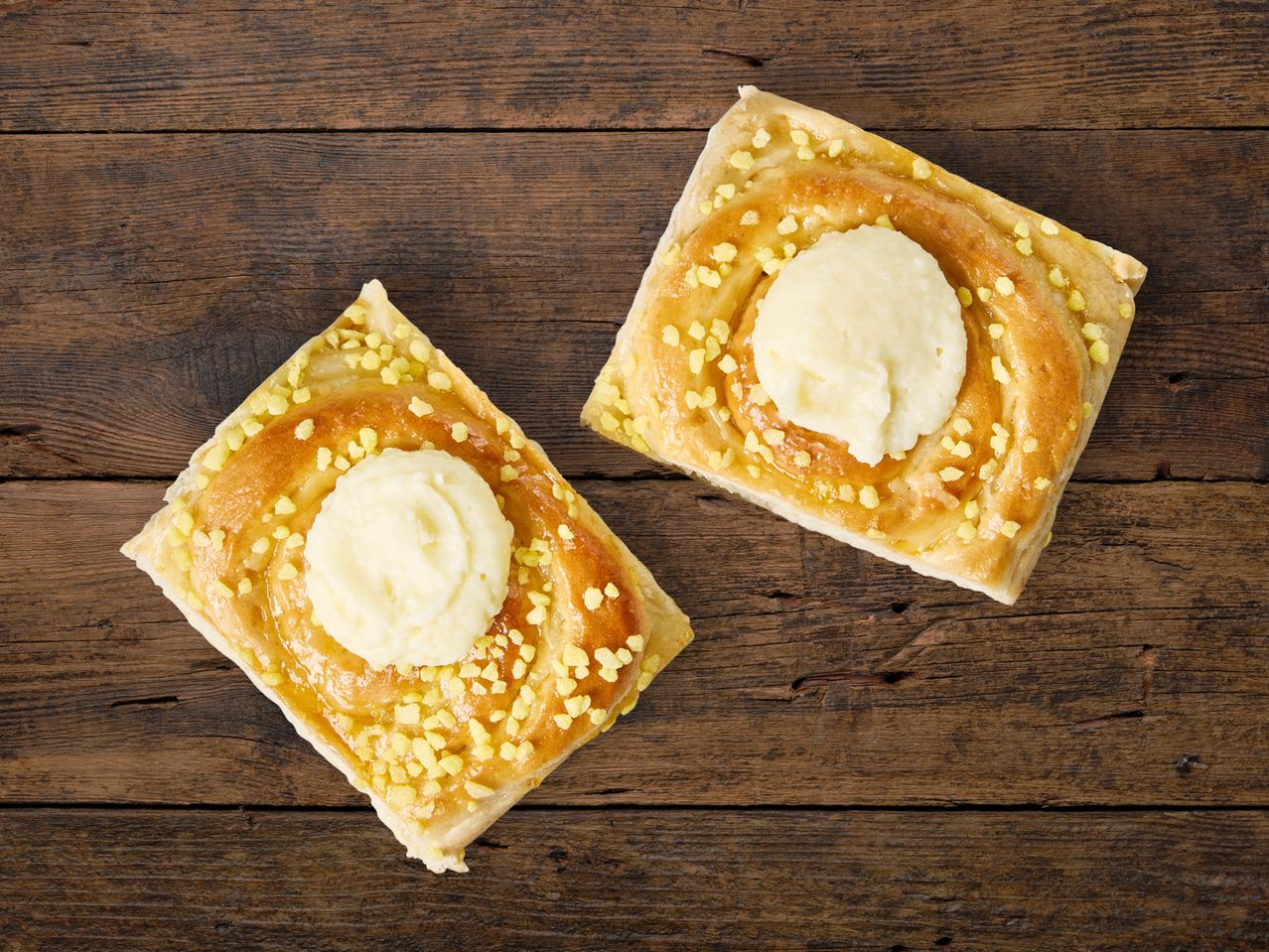 Zwei Gebäckstücke mit cremigem Käsebelag auf Holz.