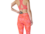 Mulher em leggings de corrida coral estampadas e sutiã desportivo, a colocar um telemóvel no bolso traseiro.