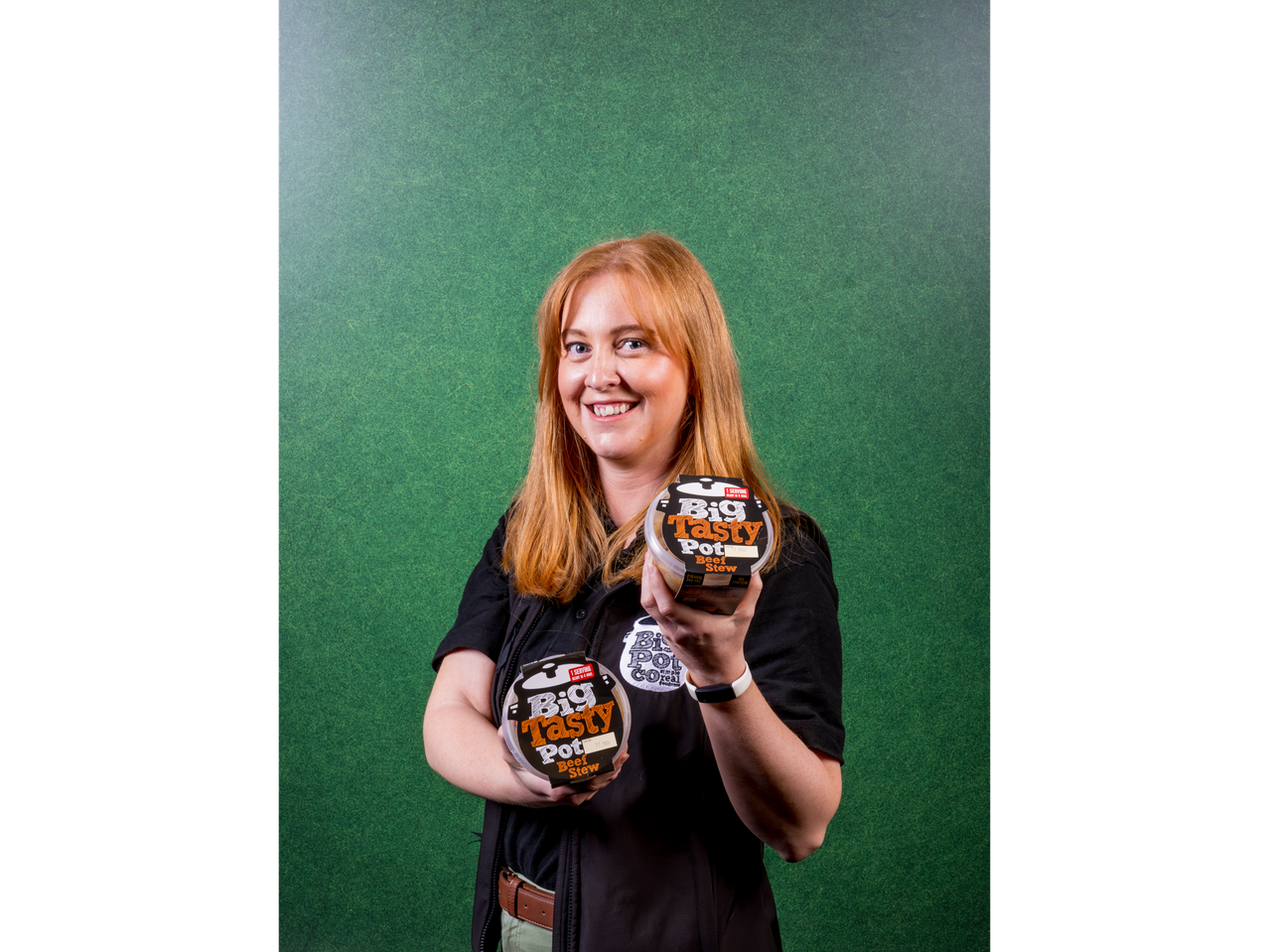 A woman holding two Big Tasty Pot Beef Stew containers against a green background.