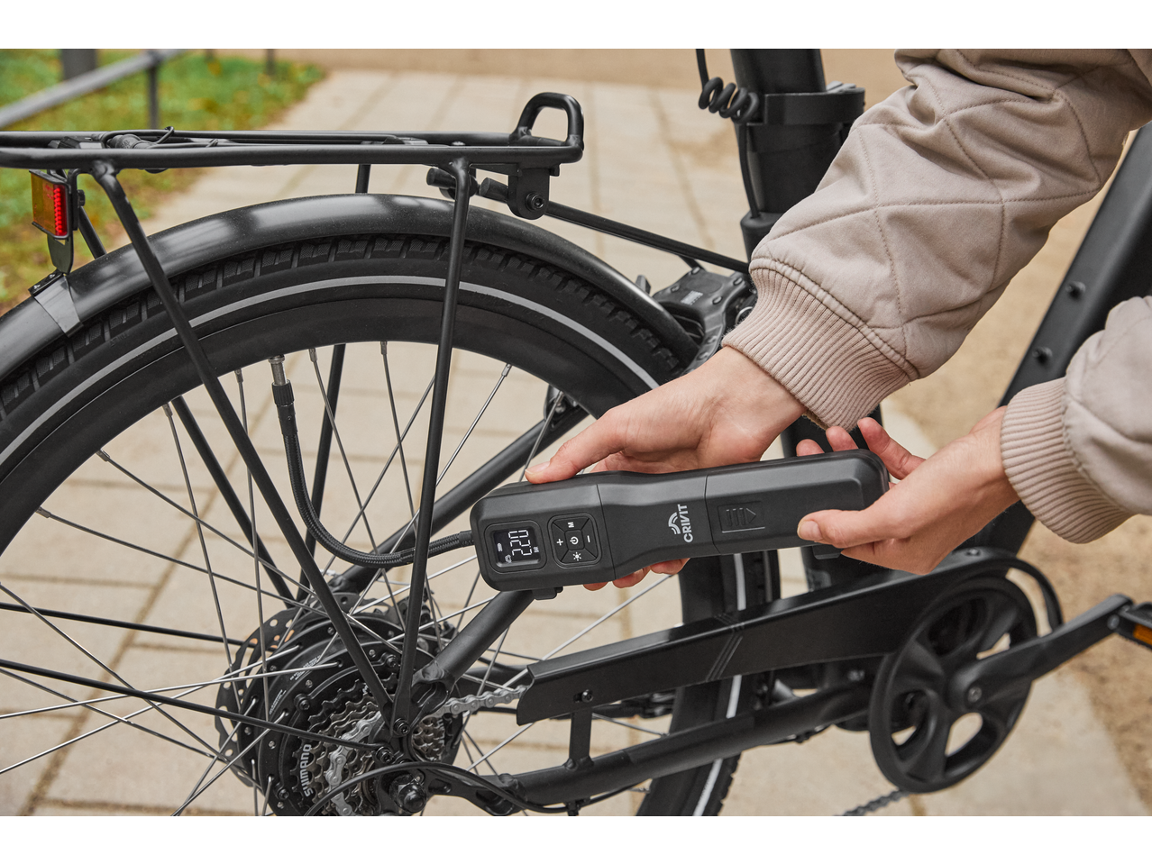 A person inflating a bicycle tire with a portable electric air pump, displaying 2.20 bar.