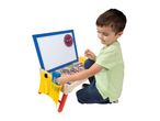 A young boy playing with a wooden activity desk featuring a whiteboard, clock, and magnetic letters.