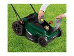 A person inserting batteries into a green lawnmower on a grassy lawn.