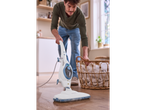 Homem a limpar o chão com o limpador a vapor Silvercrest® 2 em 1, ao lado de um cesto de roupa.