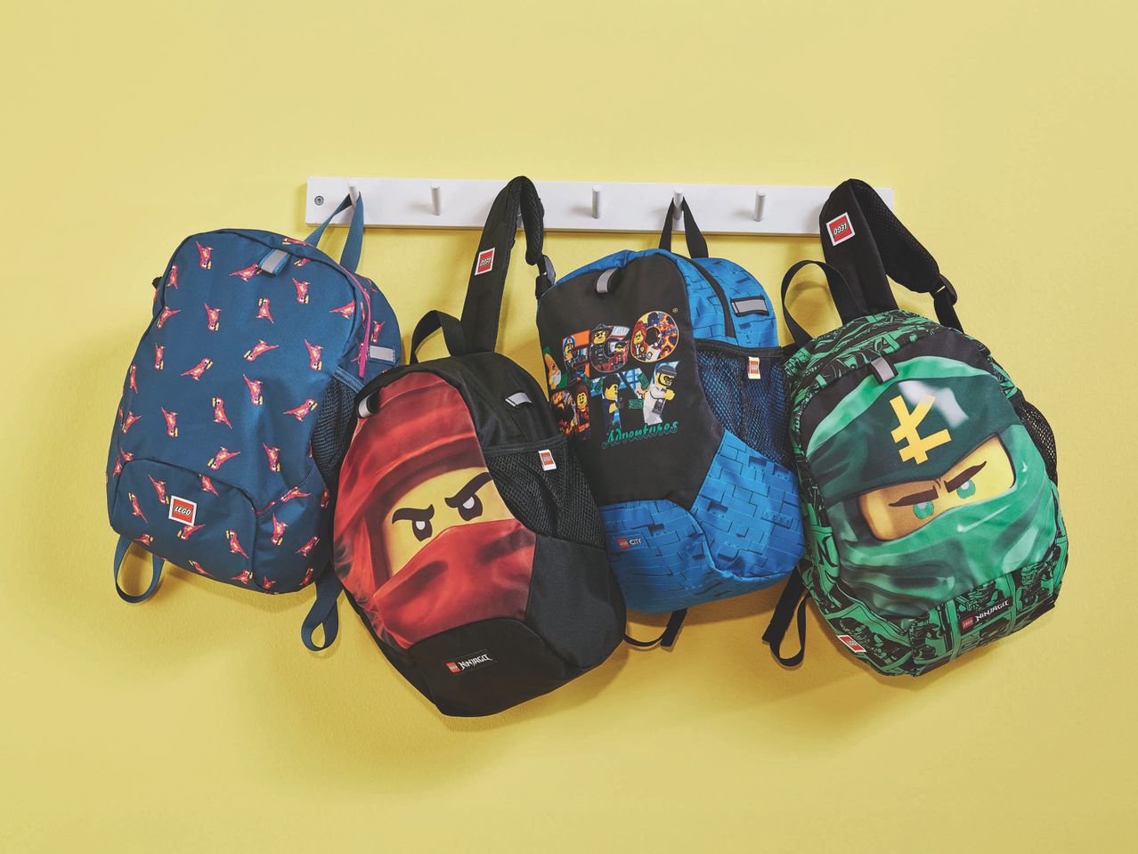 Four LEGO backpacks, including Ninjago and City themes, hanging on a white rack.