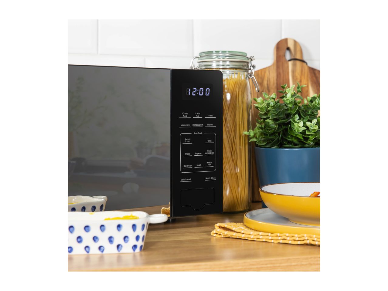 Black microwave oven with digital display showing 12:00, surrounded by kitchen items.