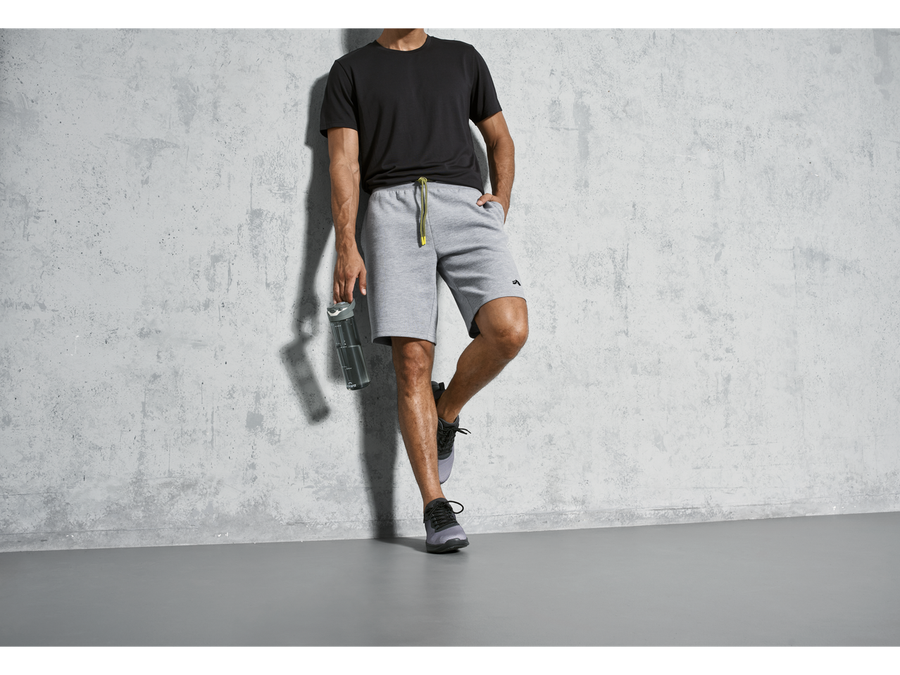 Homem de shorts, camiseta e tênis, segurando uma garrafa de água.