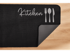 Juoda virtuvės kilimėlis su užrašu 'Kitchen' ir stalo įrankiais.