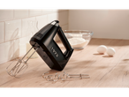 Black hand mixer with beaters and dough hooks on a wooden counter with baking ingredients.
