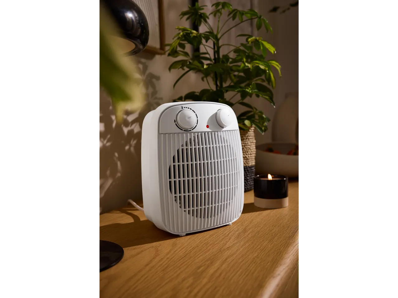 TRONIC® “Basic” fan heater on a wooden table, with a plant and candle in the background.