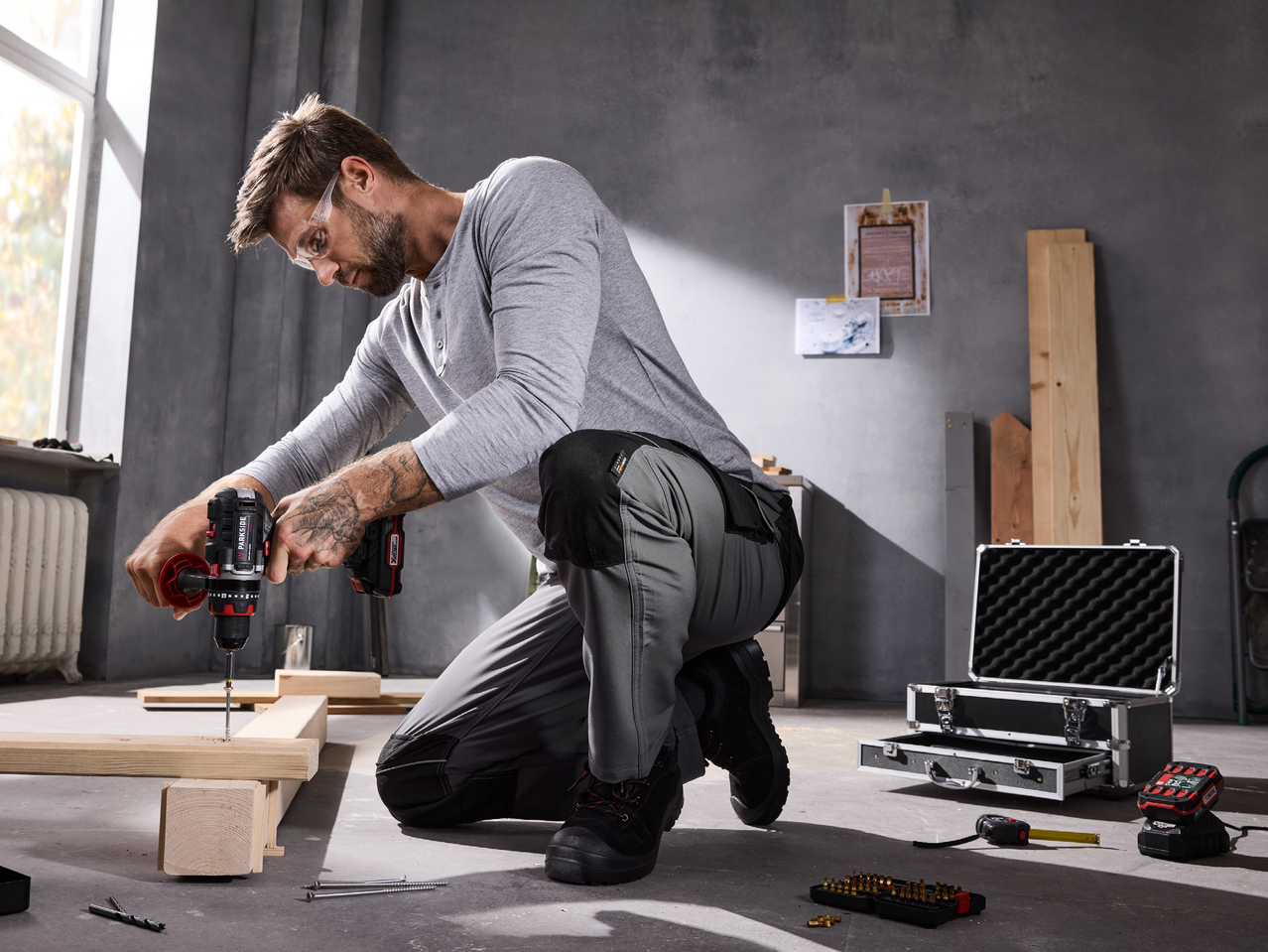 Мъж използва акумулаторна бормашина Parkside® Performance, за да пробие дървена дъска в работилница.