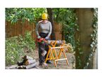 Woman using an electric chainsaw to cut logs on a sawhorse in a garden.
