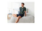 Uomo con pigiama pantaloncino blu, maglia blu con stampa a foglie tropicali. 
